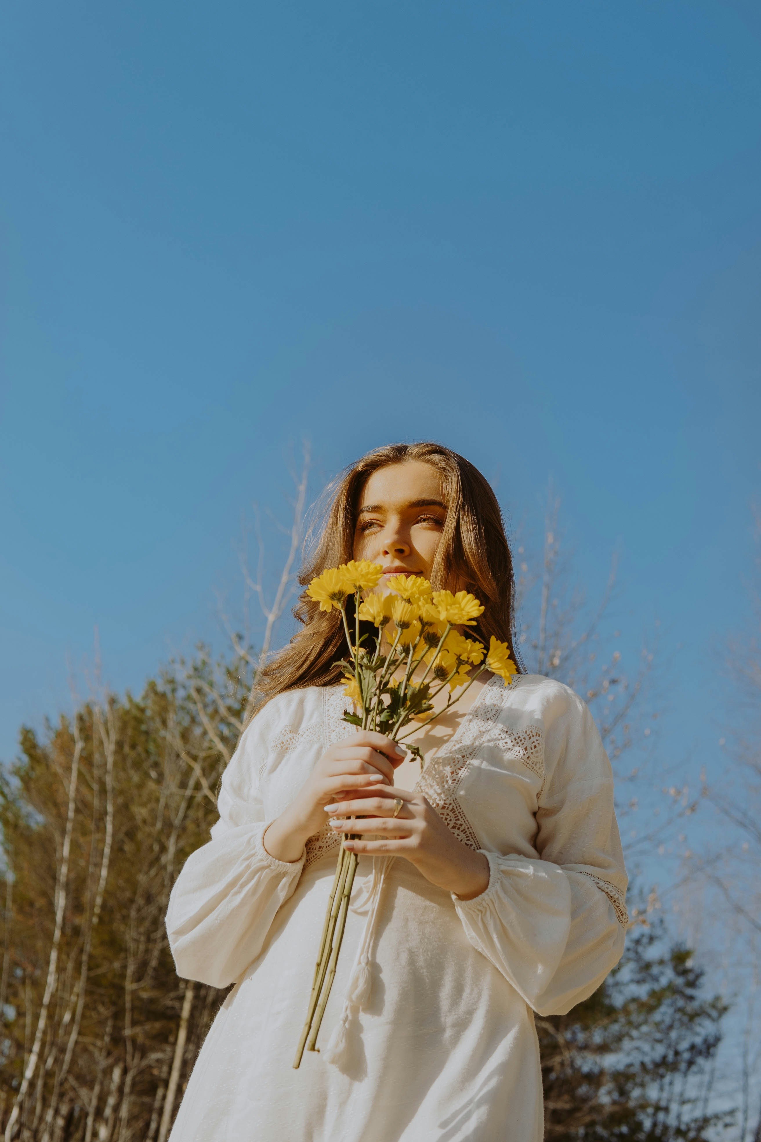 woman in white long sleeve shirt holding yellow flowers